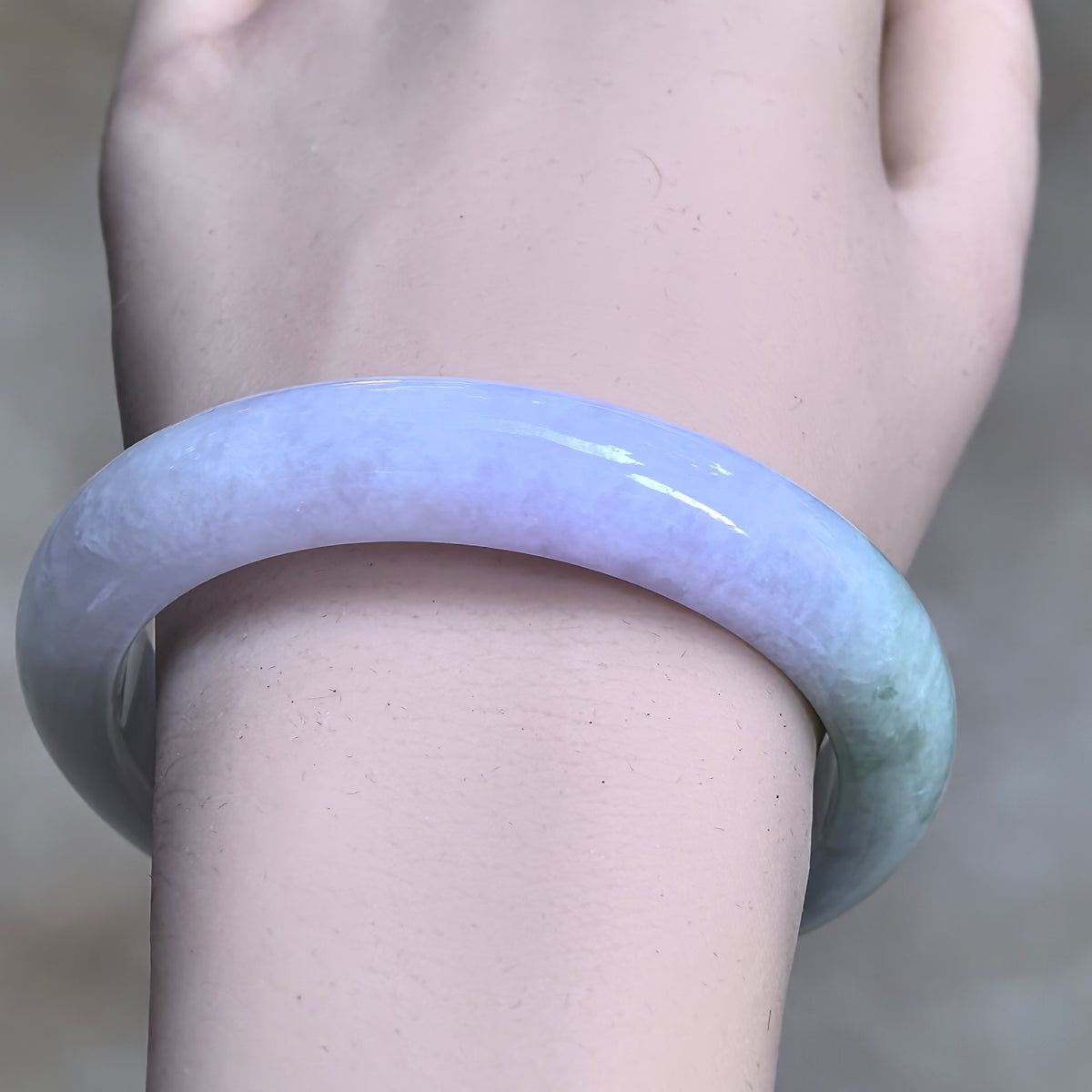 Front wrist view of a pale green and pale lavender D-shape jadeite bangle, showing its lavender front section and polished surface.