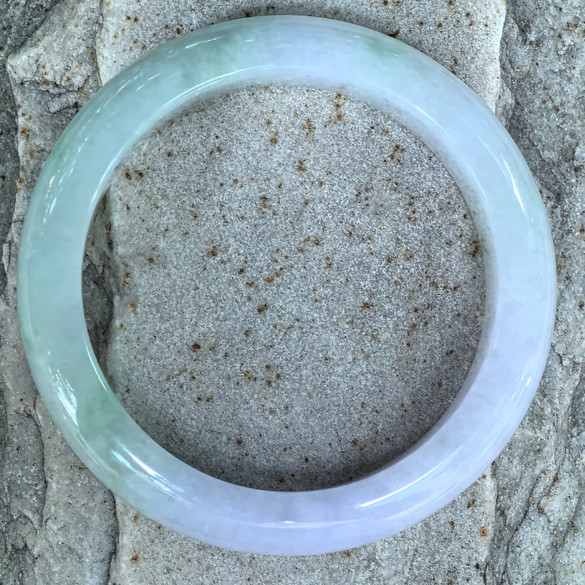 Overhead view of a glutinous jadeite D-shape bangle on stone, showing the pale green and pale lavender color sections.