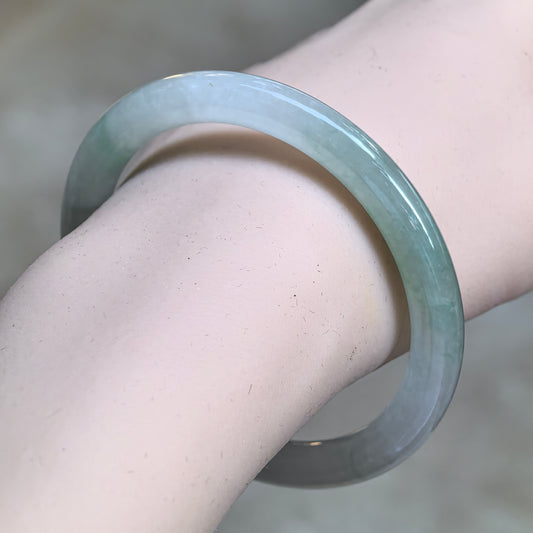 Angled wrist view of an icy glutinous light green round-bar jadeite bangle showing its slender profile and polished luster.