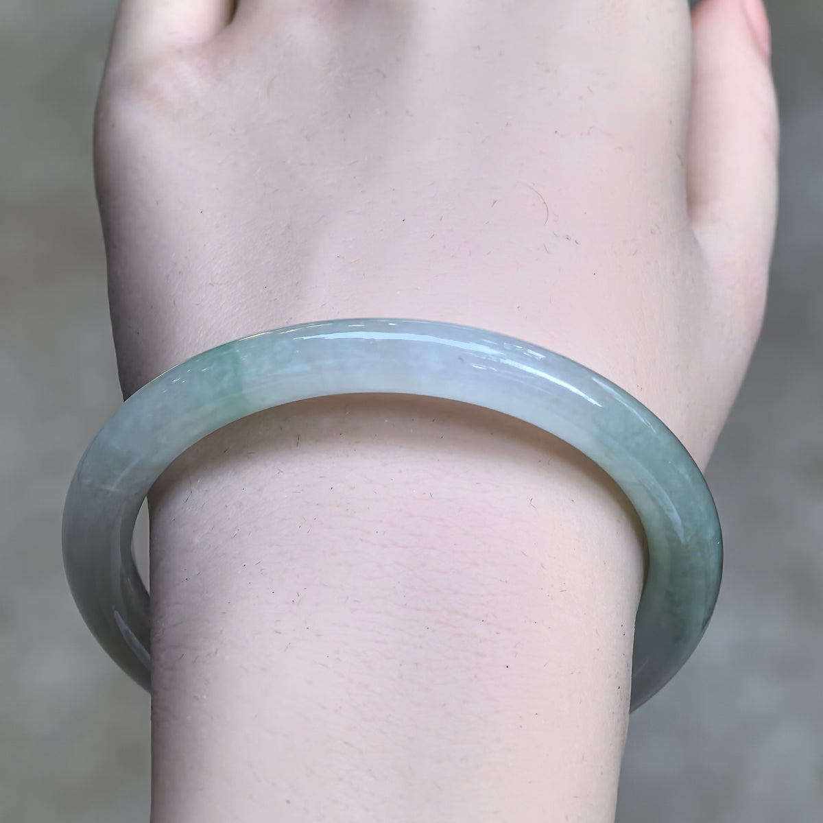 Front wrist view of a light green round-bar jadeite bangle showing its rounded contours and natural tonal variations.