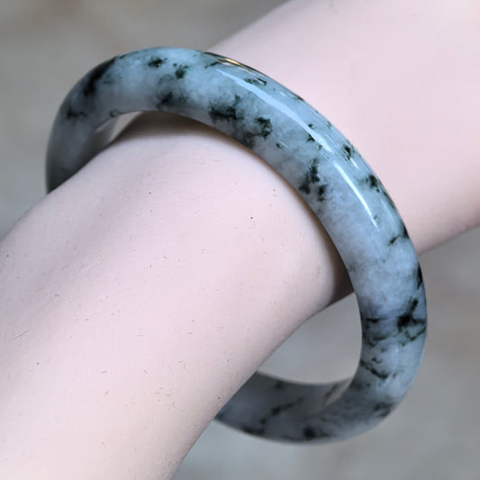 Angled wrist view of a glutinous D-shape jadeite bangle with deep green floating patterns across a pale green base.