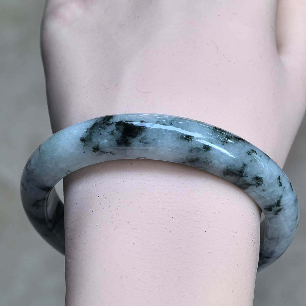 Front wrist view of a D-shape jadeite bangle showing darker green clusters, branching patterns, and a polished exterior.