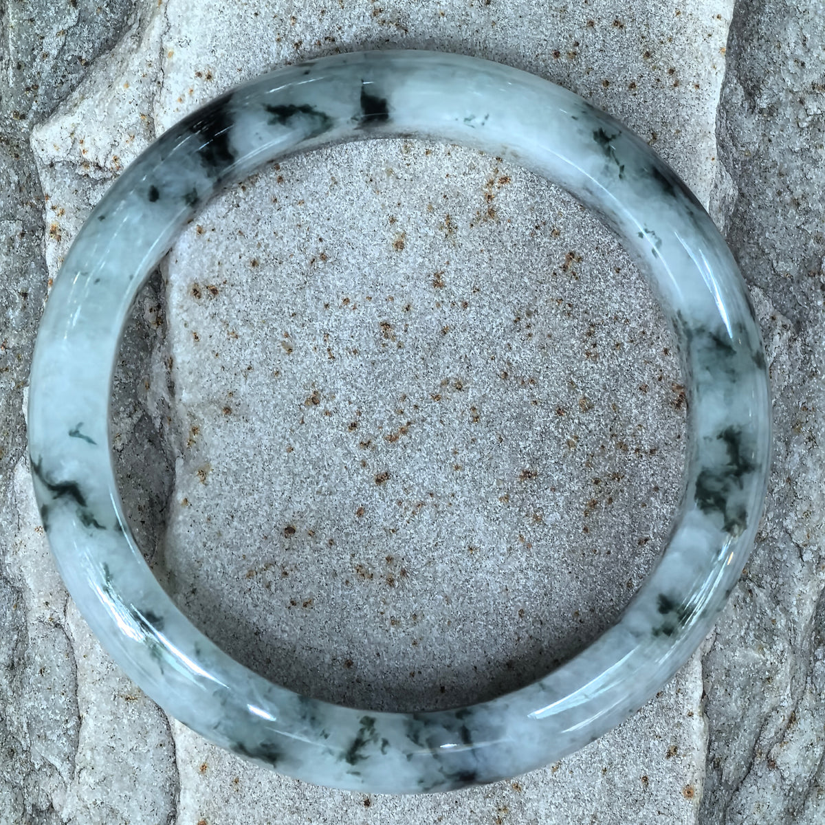 Overhead view of a pale green D-shape jadeite bangle on stone, showing the distribution of deep green floating patterns around the band.