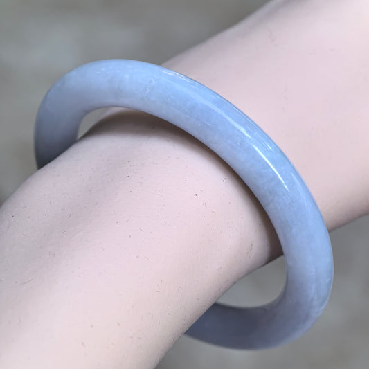 Angled wrist view of a very pale lavender round-bar jadeite bangle with a faint blue-lavender tone and a polished finish.