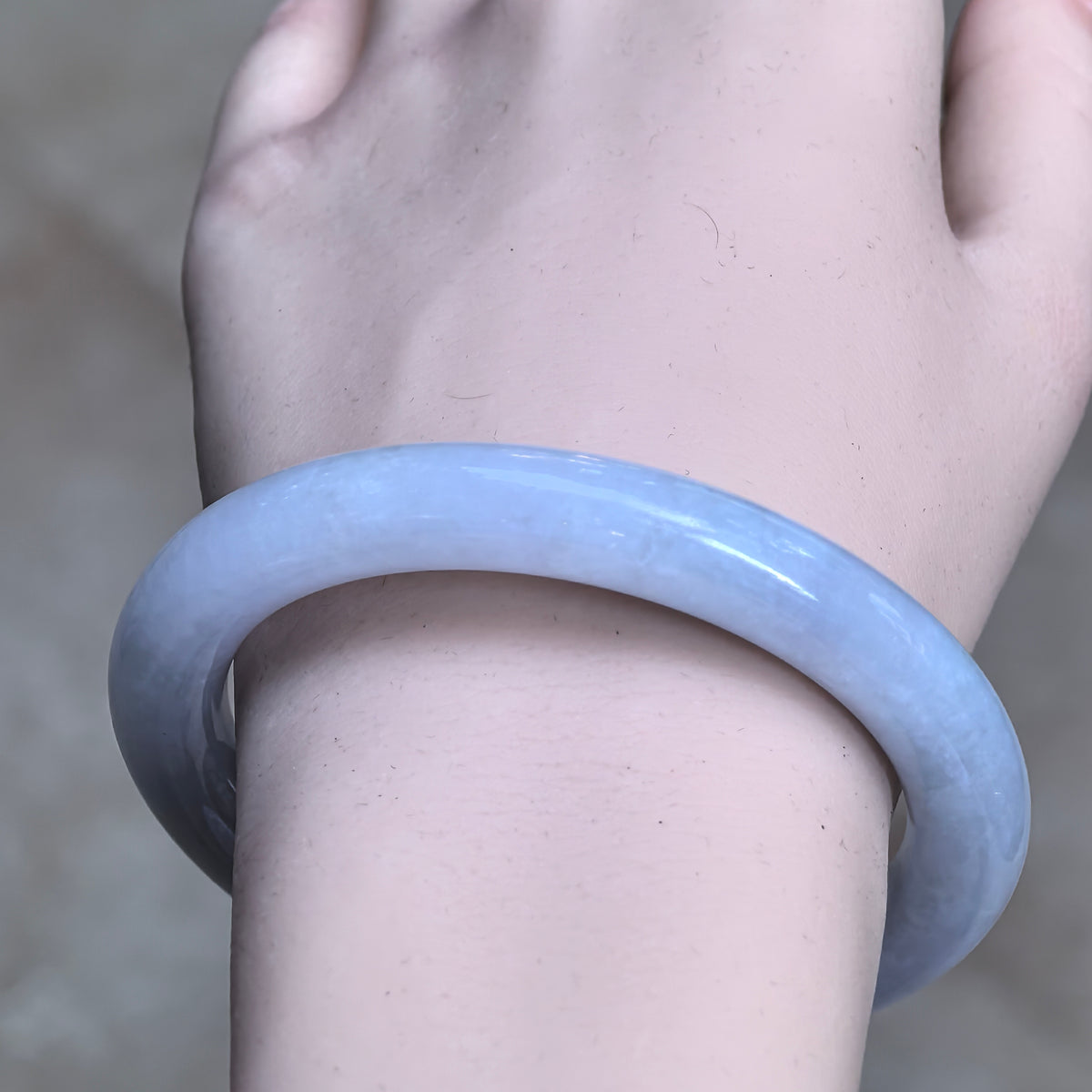 Front wrist view of a pale lavender round-bar jadeite bangle showing its rounded profile and softly varied texture.