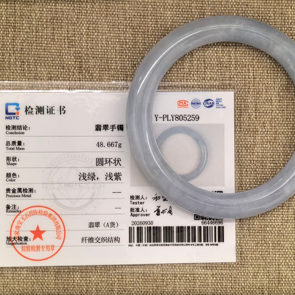 Pale lavender round-bar jadeite bangle displayed with its matching NGTC certificate on a woven background.