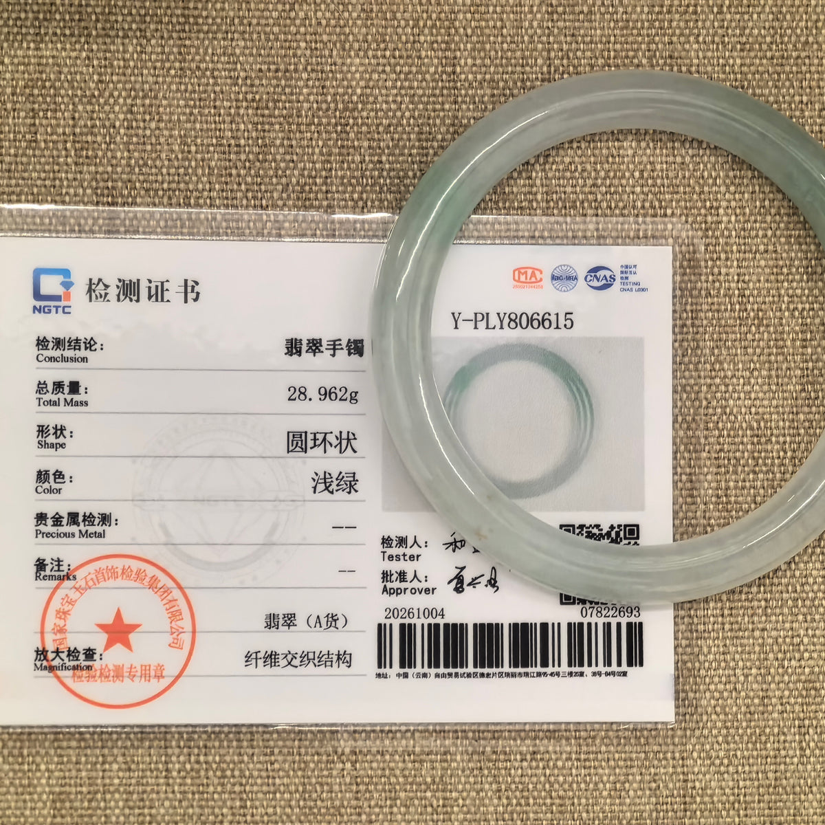 Light green round-bar jadeite bangle displayed with its matching NGTC certificate on a woven background.