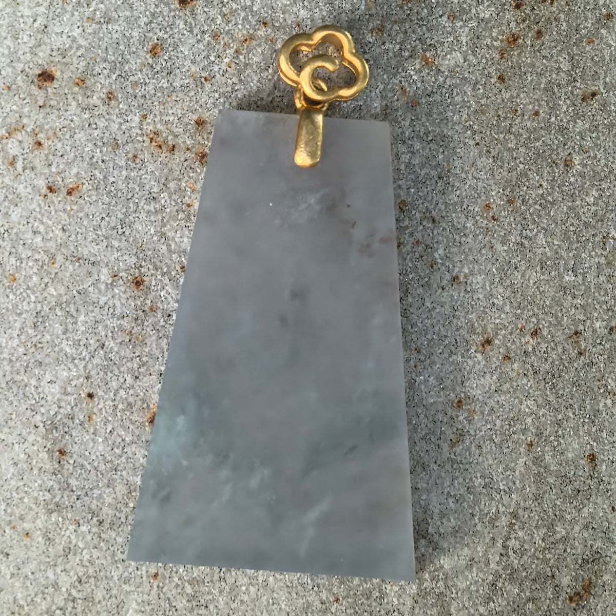 Front view of the pale blue jadeite Plain Plaque Pendant on stone, with misty cotton-like inclusions beneath an 18K gold cloud-shaped bail.