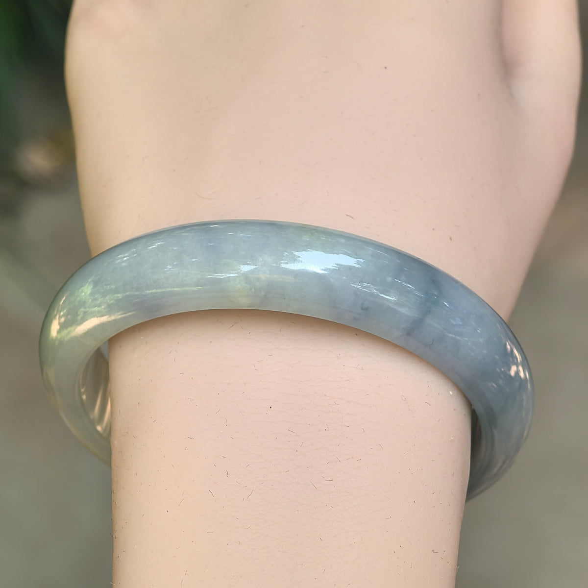 Front wrist view of a denim blue jadeite D-shape bangle, showing lighter tonal areas and darker floating patterns across the band.