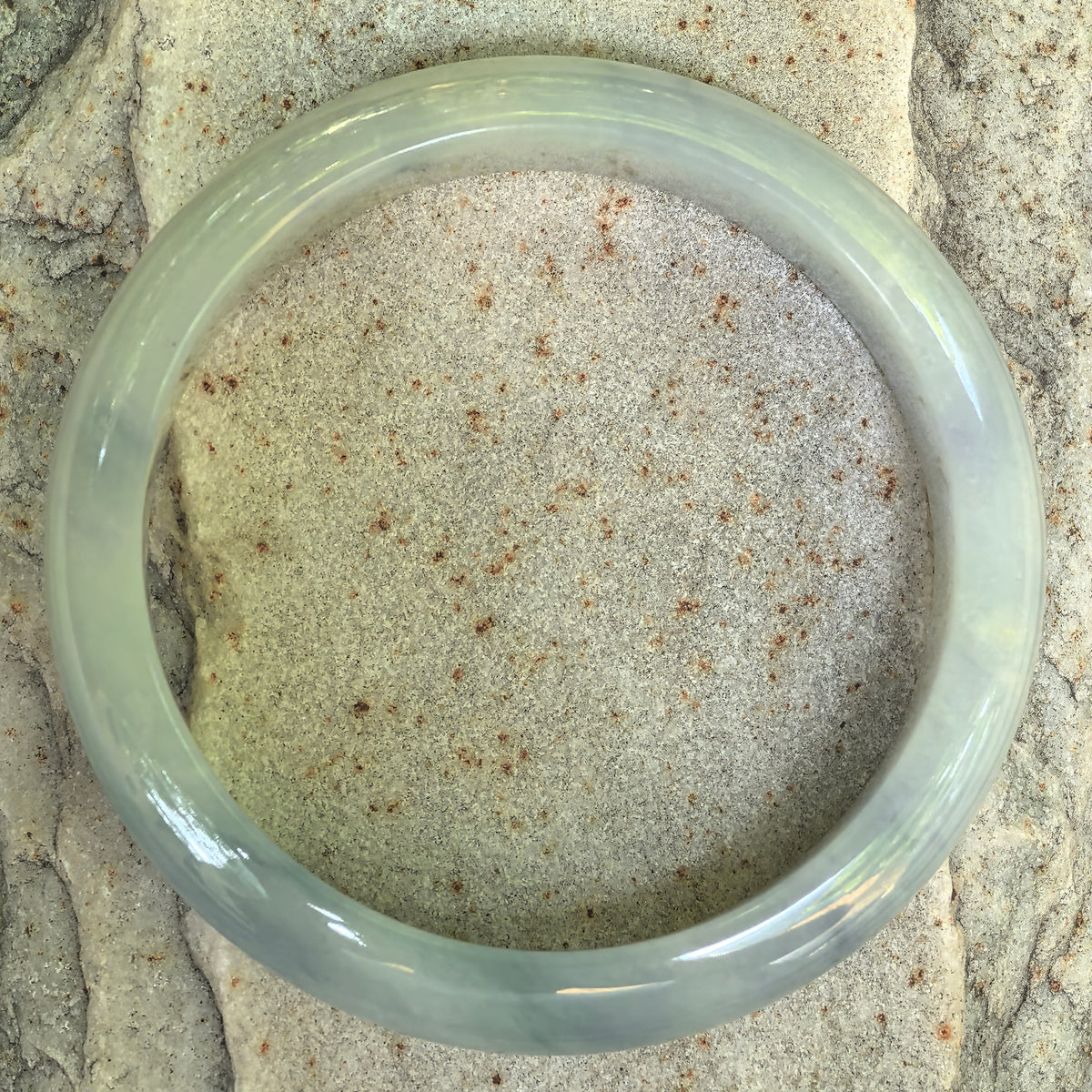 Overhead view of a denim blue glutinous jadeite D-shape bangle on textured stone, showing its circular outline and natural tonal variations.