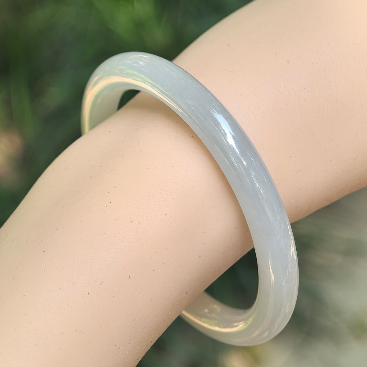 Angled wrist view of a white jadeite round-bar bangle, showing its slender profile and softly rounded curves.