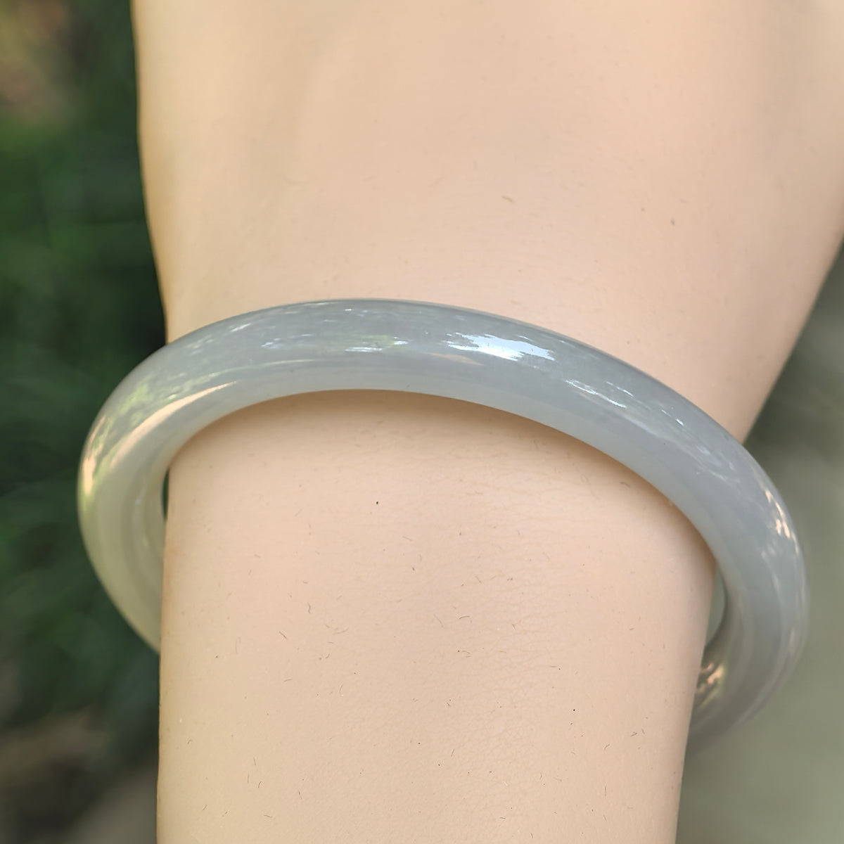 Front wrist view of a white icy glutinous jadeite slim round-bar bangle with a subtle pale green undertone and polished surface.