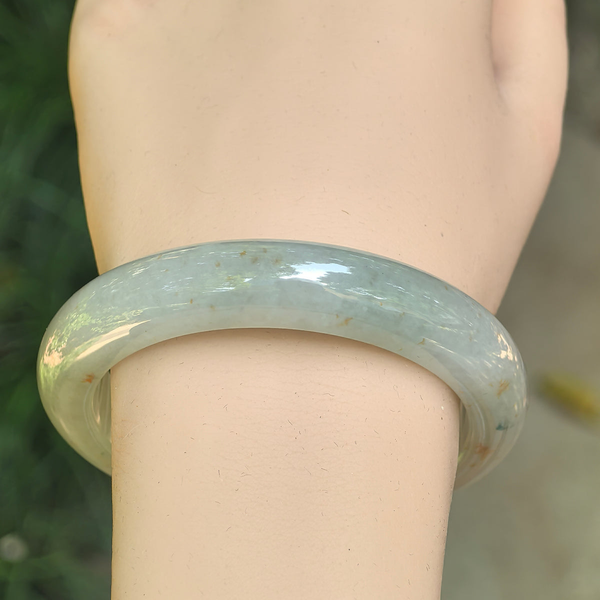 Front wrist view of the pale green D-shape jadeite bangle, showing scattered golden-brown flecks and its polished outer curve.