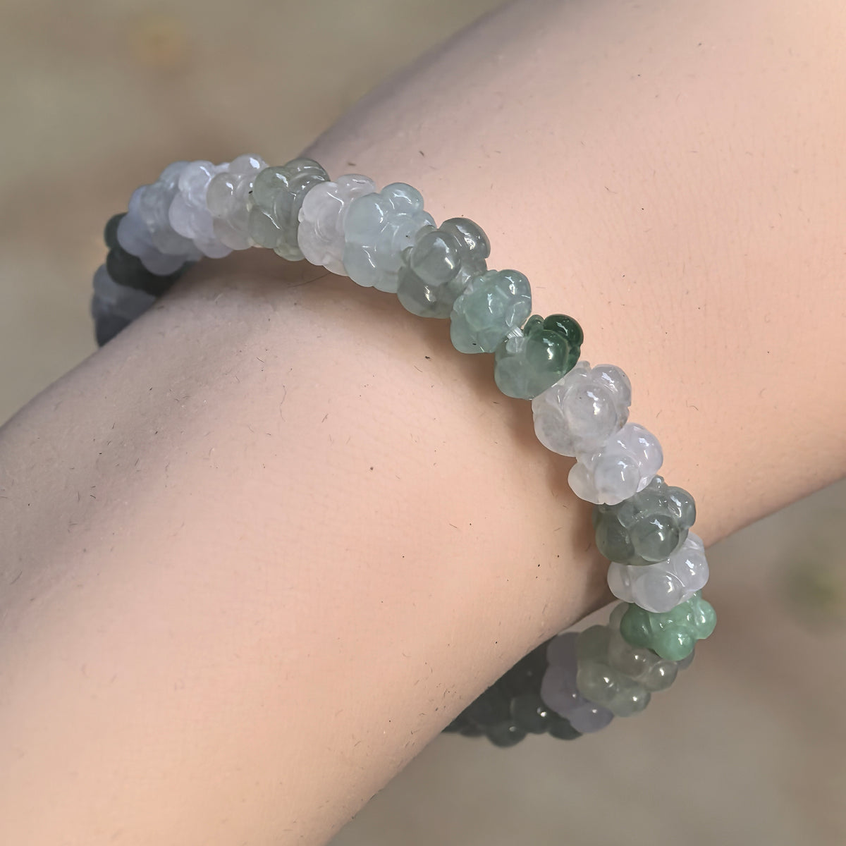 Fine glutinous light green and white jadeite lotus bead bracelet worn at an angle on the wrist, showing rounded petal carvings and varied bead sizes.