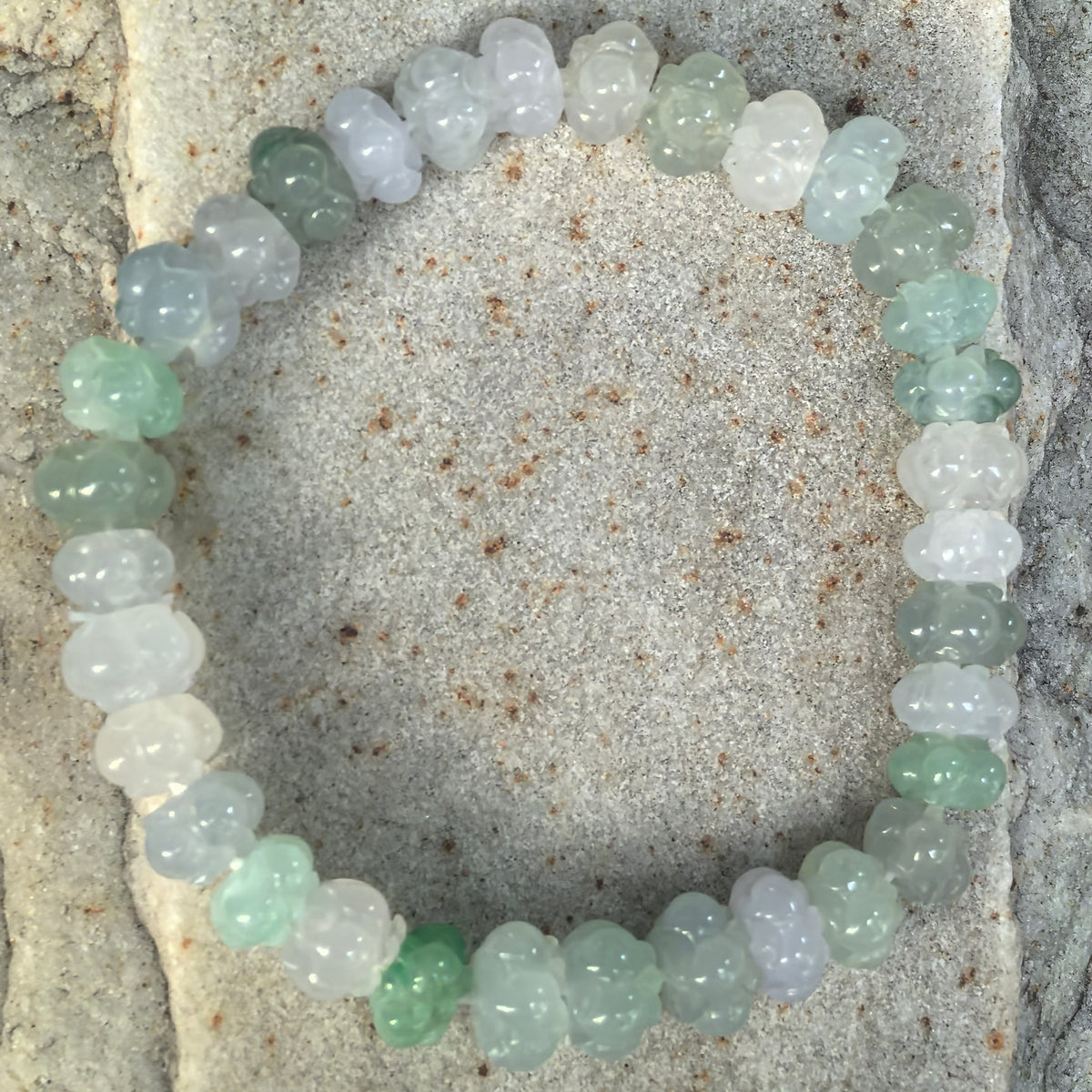 Overhead view of a light green and white jadeite lotus bead bracelet on stone, showing the full loop and variations in bead shape and color.