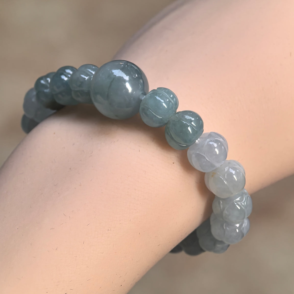 Fine glutinous light green gradient jadeite lotus bead bracelet worn at an angle on the wrist, showing the round focal bead and its natural color line.