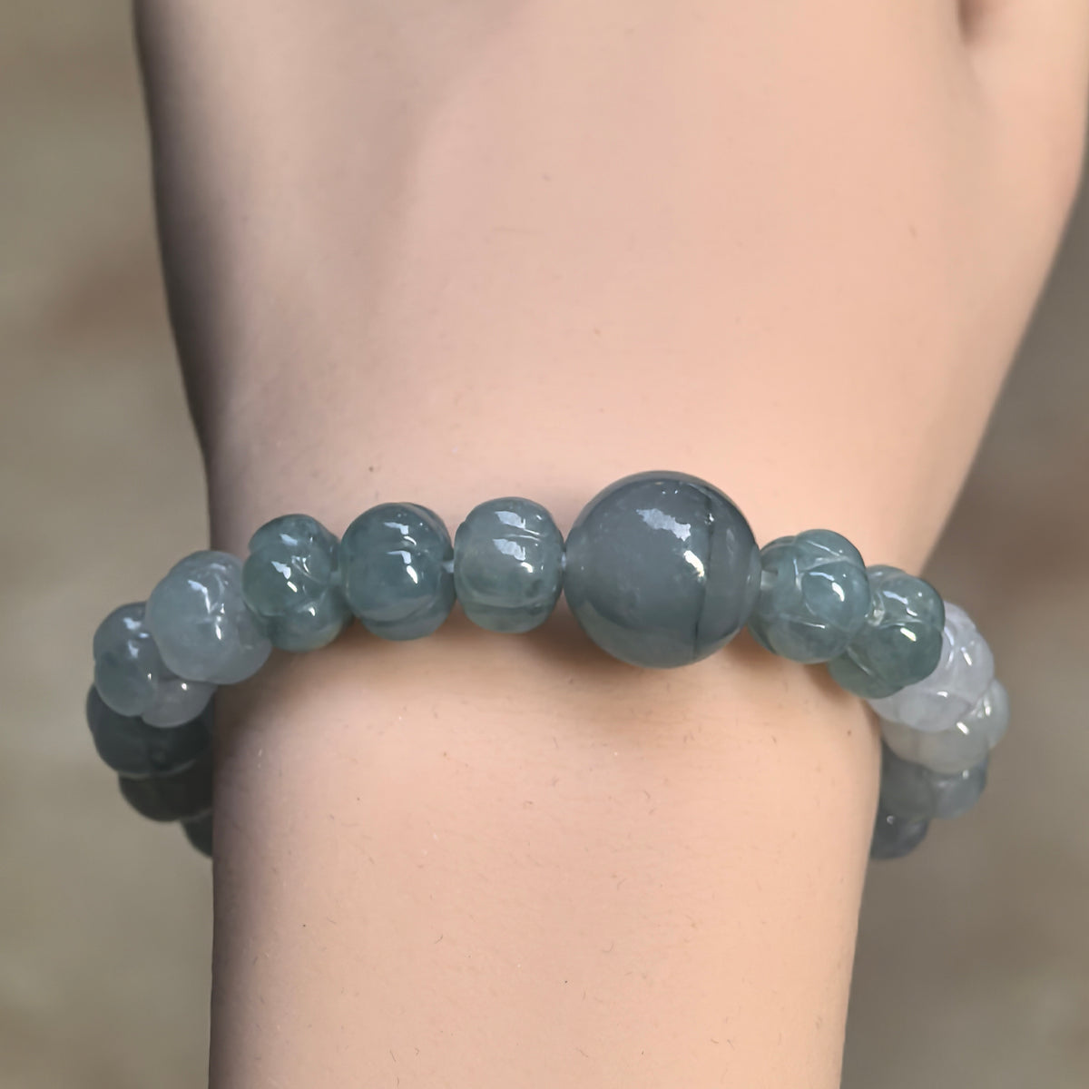 Front wrist view of a light green gradient jadeite bracelet with lotus-carved beads surrounding a larger smooth round focal bead.