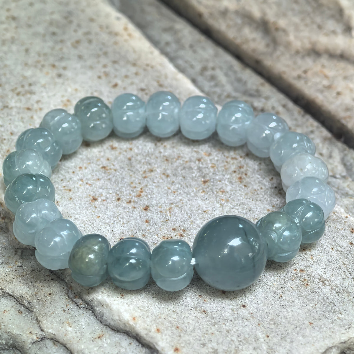 Angled close-up of a jadeite lotus bead bracelet on stone, showing the green color variation and natural color line in the round focal bead.