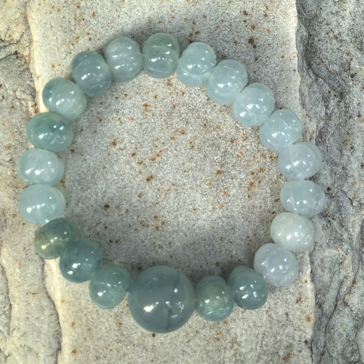 Overhead view of a light green gradient jadeite lotus bead bracelet arranged on stone, showing the petal carvings and round focal bead.