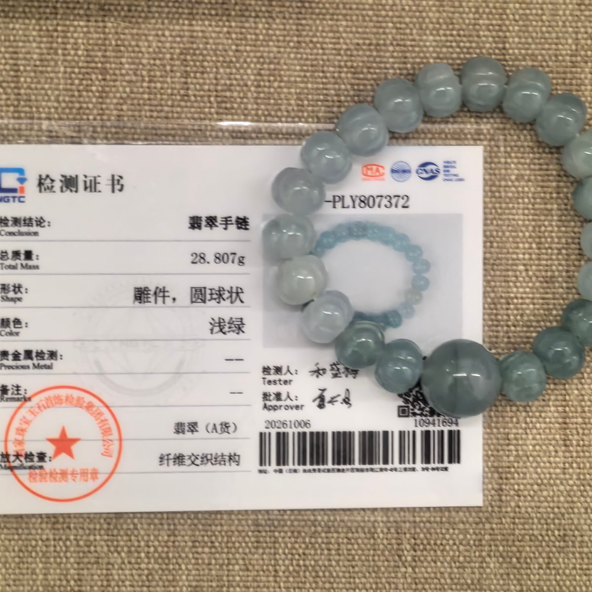 Light green gradient jadeite lotus bead bracelet displayed over its matching NGTC certificate on a woven background.