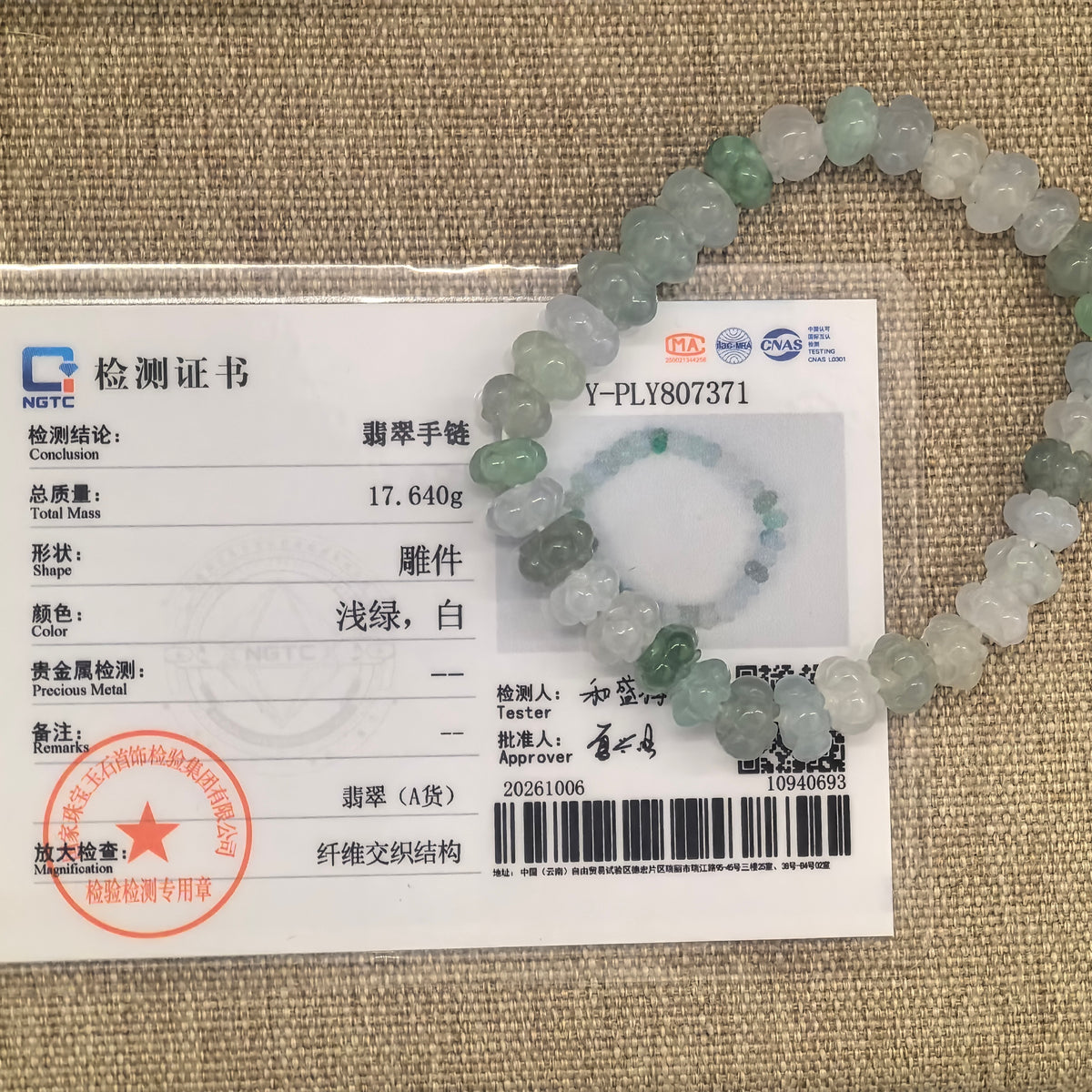 Light green and white jadeite lotus bead bracelet displayed over its matching NGTC certificate on a woven background.