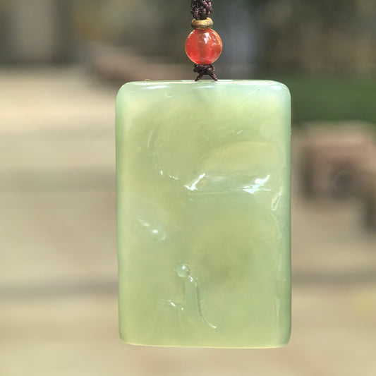 Lake green Hetian jade Enlightenment plaque pendant hanging from a cord, showing softly rounded corners and flowing carved forms.