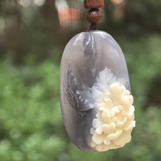 Smoky purple Hetian jade pendant hanging from a cord, showing a carved bird beside a raised white quartzite flower.