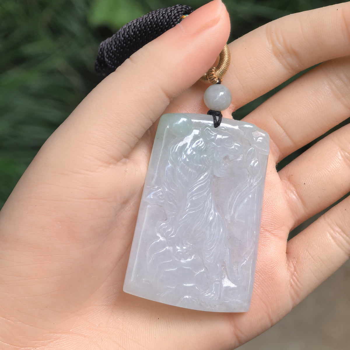 Pale green jadeite tiger plaque pendant resting in a palm, showing its rectangular outline and detailed animal carving.