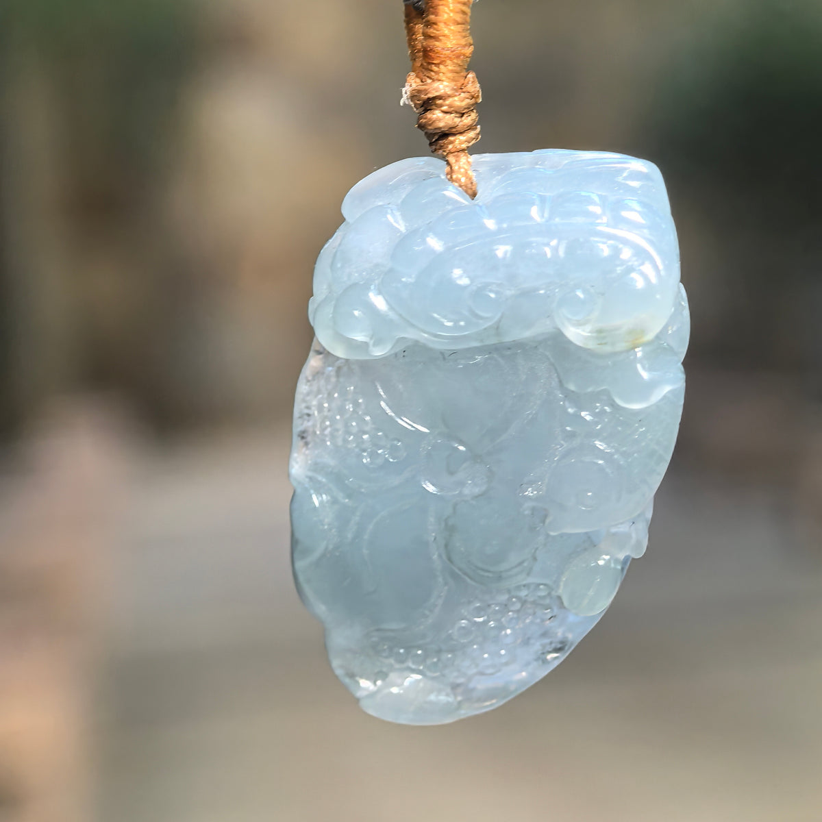 Icy glutinous blue lotus jadeite pendant hanging from a cord, showing its translucency, rounded relief carving and curling accents.