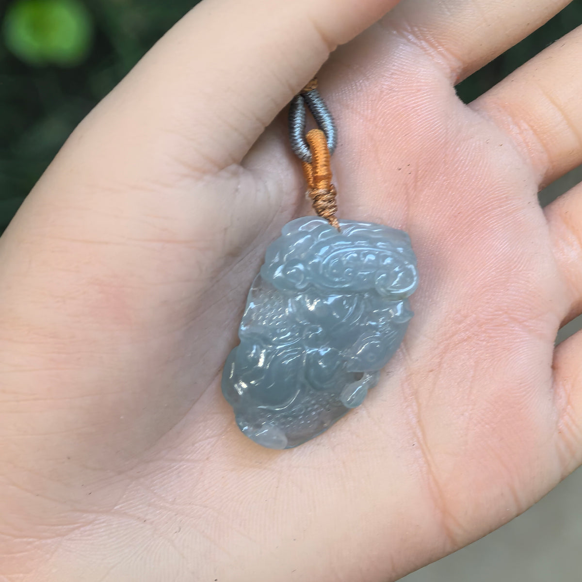 Blue lotus jadeite pendant resting in a palm, showing the carved petals, seed pods and irregular outline.