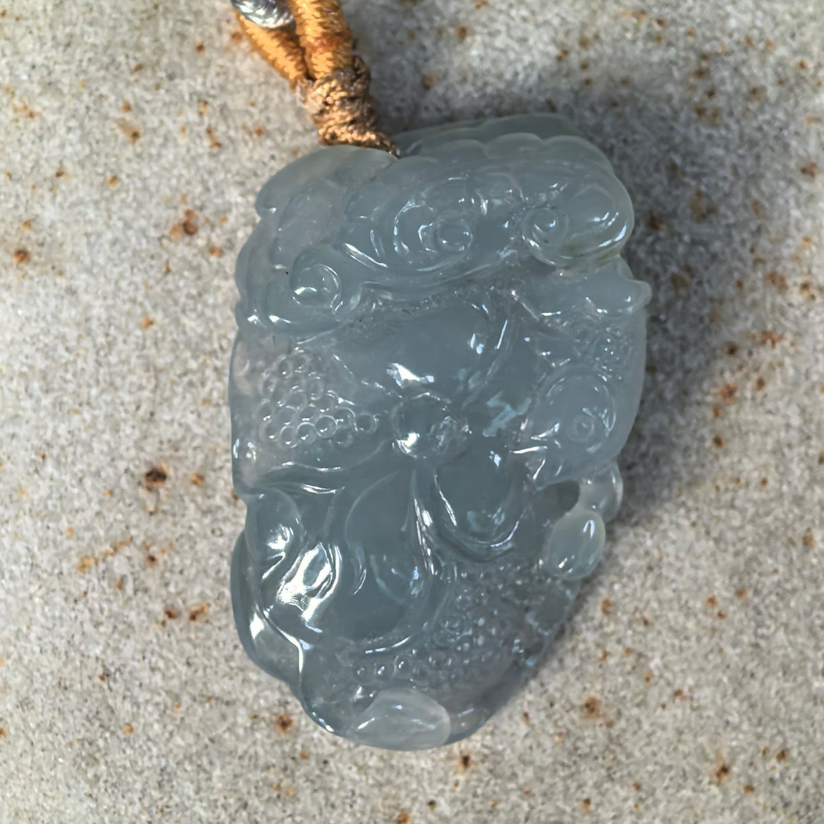 Front view of a blue lotus jadeite pendant on stone, showing the full relief composition and patterned seed pods.