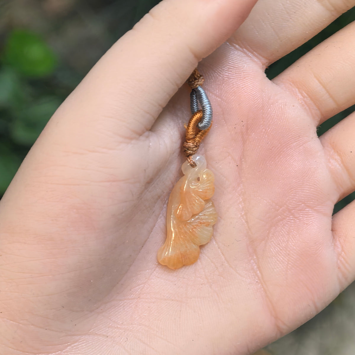 Fine glutinous yellow jadeite ginkgo leaf pendant resting in a palm, showing its compact size and slender curved silhouette.