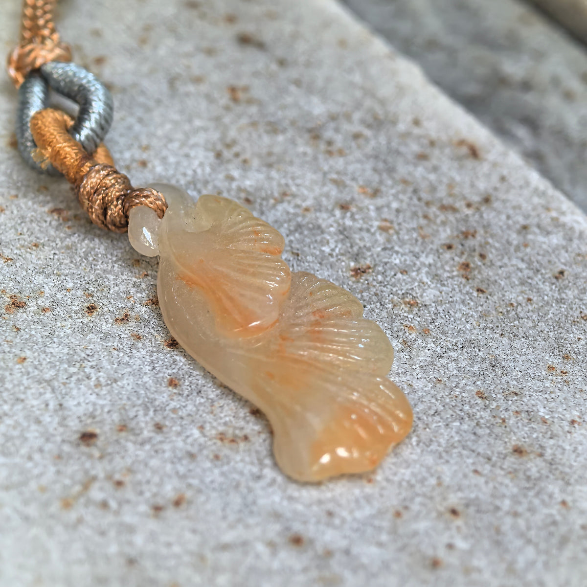 Angled close-up of a yellow jadeite ginkgo leaf pendant on stone, highlighting layered relief carving, leaf veins and its side profile.