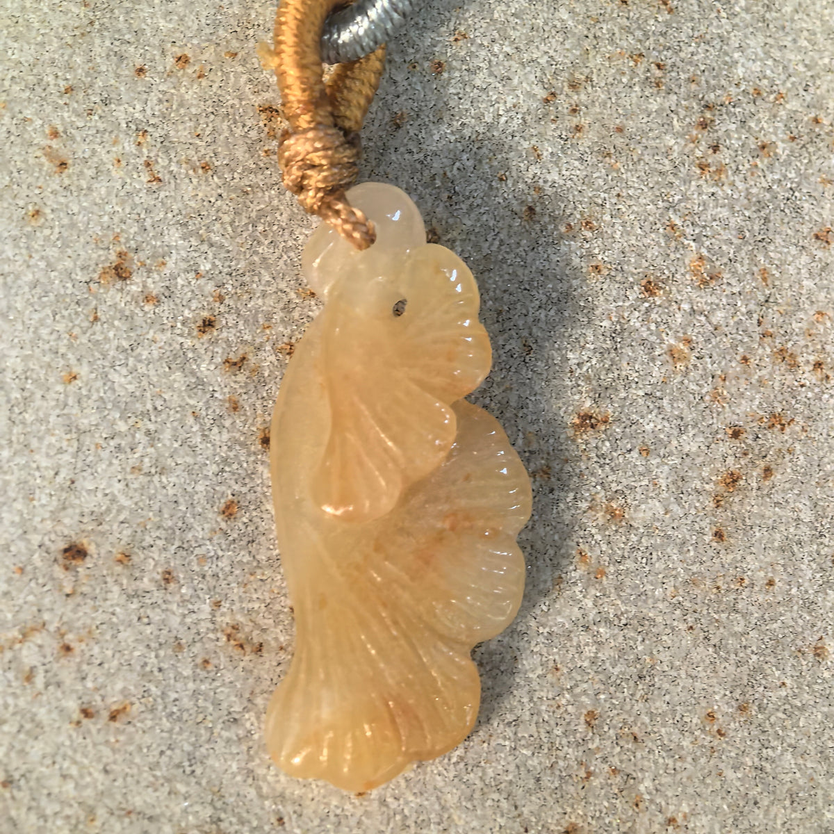 Front view of a yellow jadeite ginkgo leaf pendant on stone, showing overlapping fan-shaped leaves and gentle color variations.