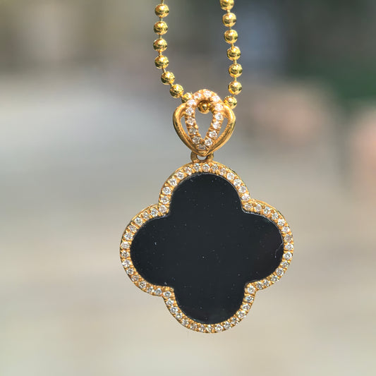 Black jadeite four-leaf clover pendant hanging from a bead chain, showing its 18K gold setting, diamond border and openwork bail.