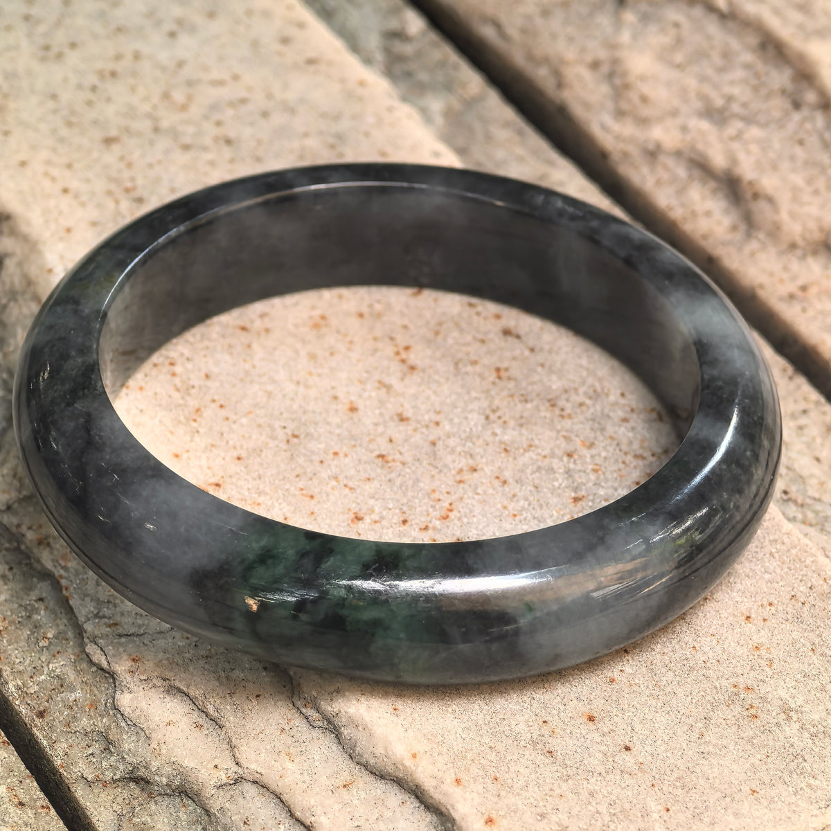 Close-up of a black-and-green jadeite D-shape bangle showing the polished surface, green section, and natural stone texture.