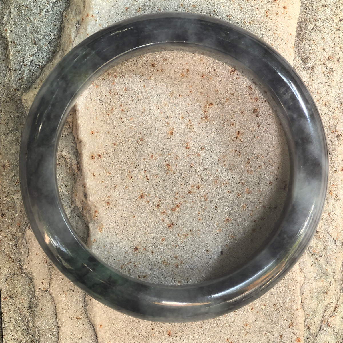 Top view of a glutinous black-and-green Burmese jadeite D-shape bangle showing its natural mottled color pattern.