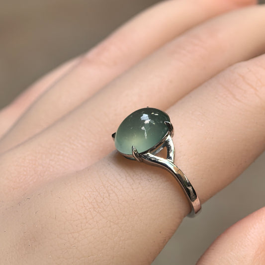 Angled view of an icy light green oval jadeite ring worn on a finger, showing the domed cabochon and curved Pt950 platinum shoulder.