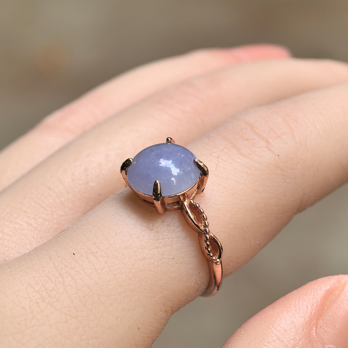 Angled view of a purple jadeite ring worn on a finger, showing the domed cabochon and openwork shoulder details with beaded edges.