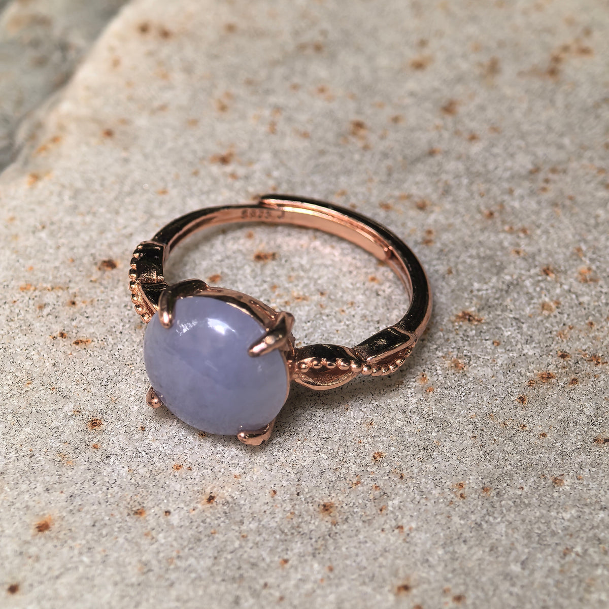 Angled close-up of a purple jadeite ring on a stone surface, showing the twisted shoulder design and adjustable open ring band.