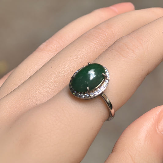 Angled view of an oval gray-green jadeite halo ring worn on a finger, showing the domed cabochon and slim S925 sterling silver band.