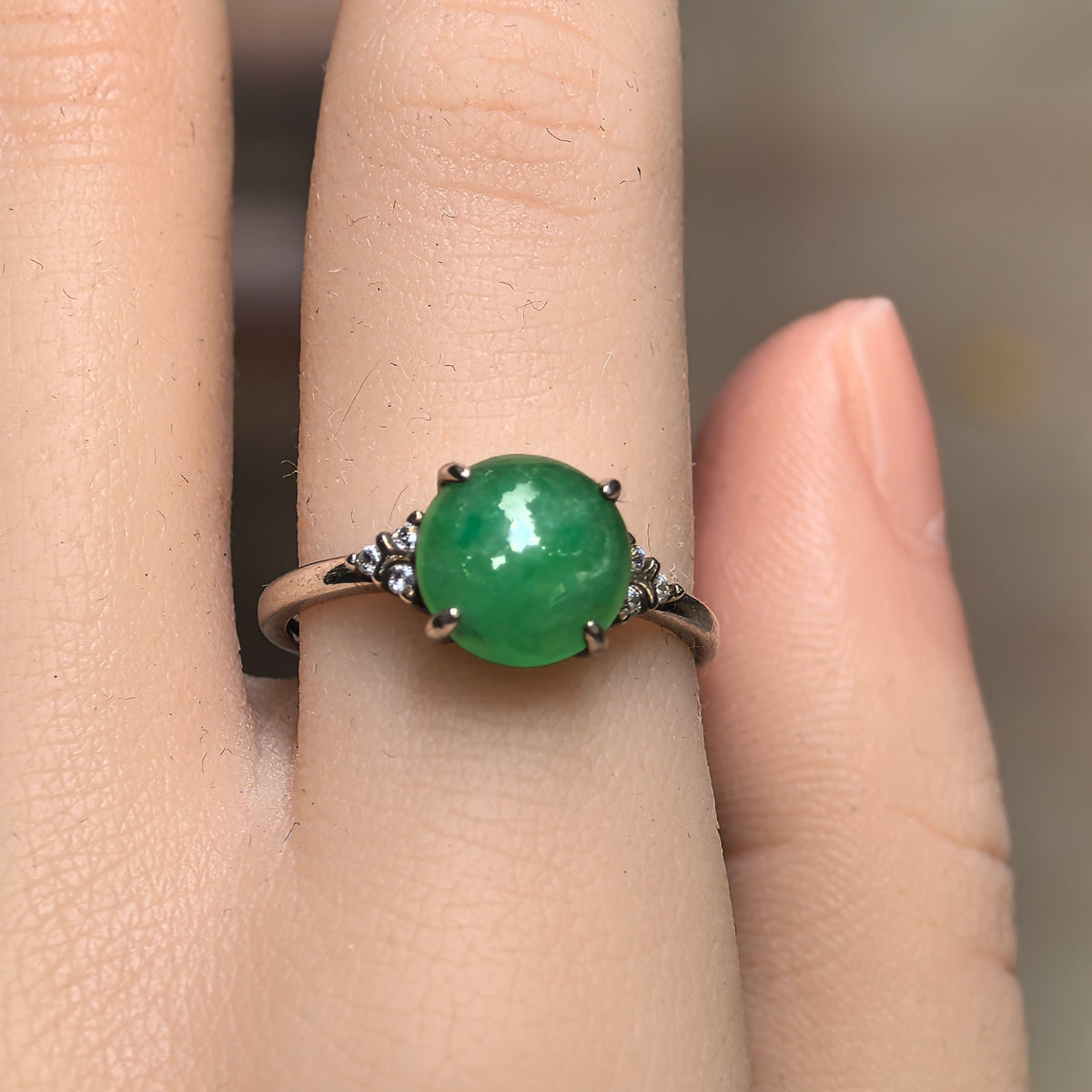 Front view of a glutinous green jadeite ring worn on a finger, with a round cabochon and clusters of clear accent stones on both sides.
