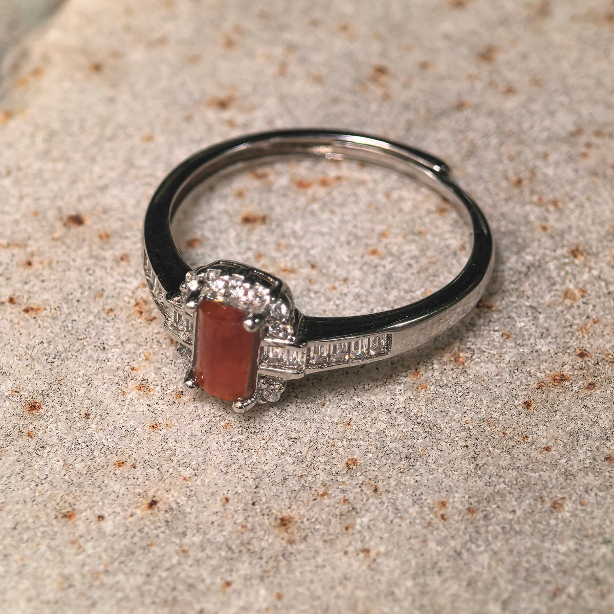 Angled view of a rectangular jadeite ring on a stone surface, showing the shoulder accents and adjustable open silver band.