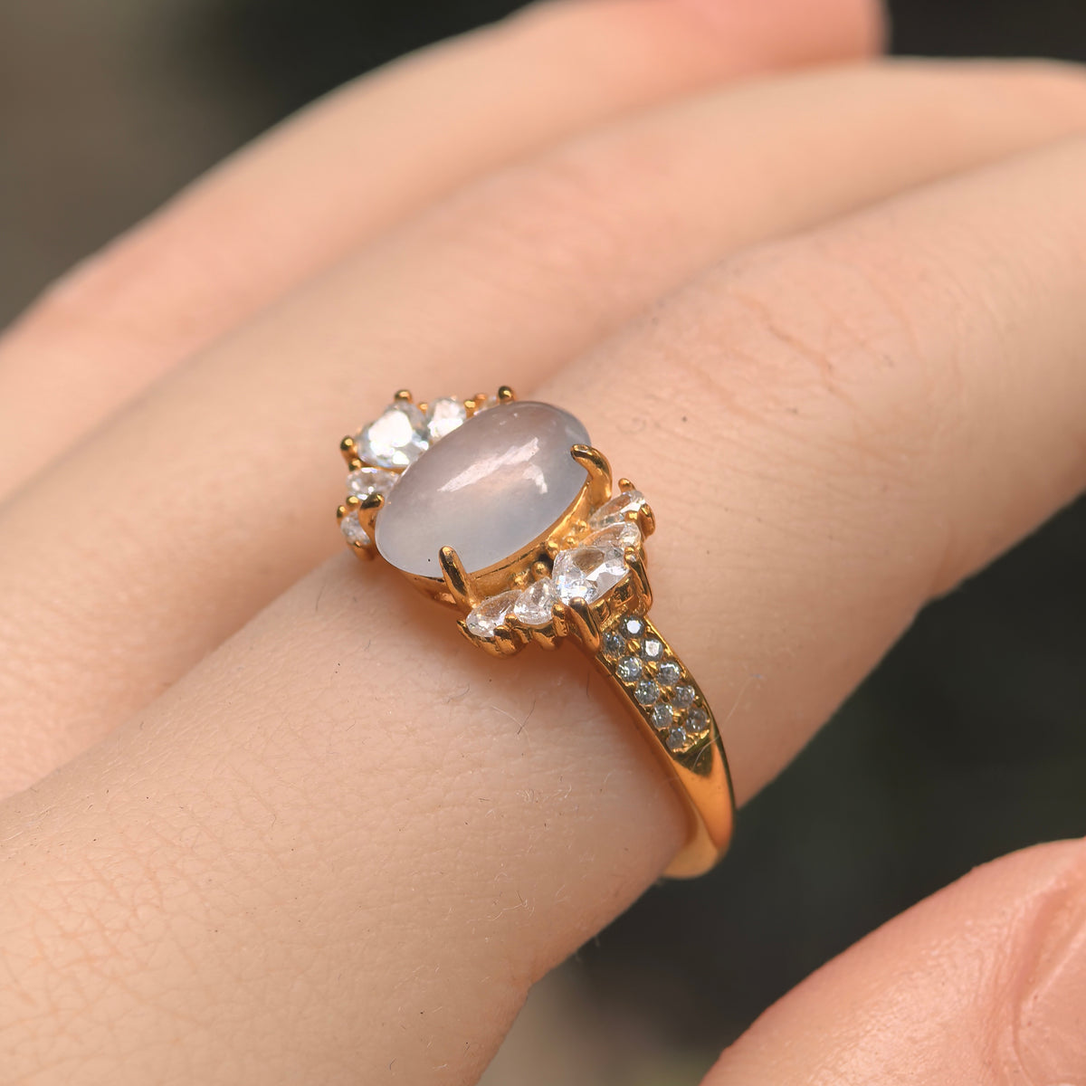 Angled view of a white oval jadeite ring worn on a finger, with a gold-tone silver setting and clear side accents.