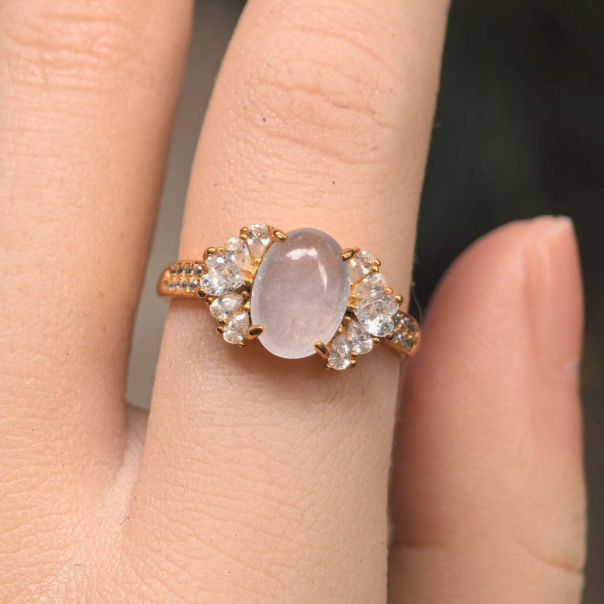 Front view of a white jadeite ring worn on a finger, showing fan-shaped clusters of clear accent stones on both sides.