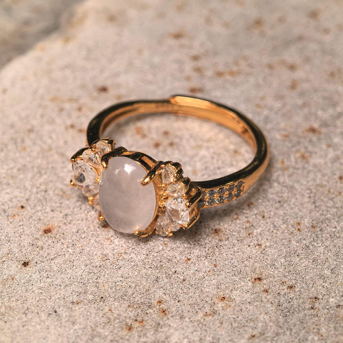 Angled view of a white jadeite ring on a stone surface, showing the prong setting, clear accents and adjustable band.
