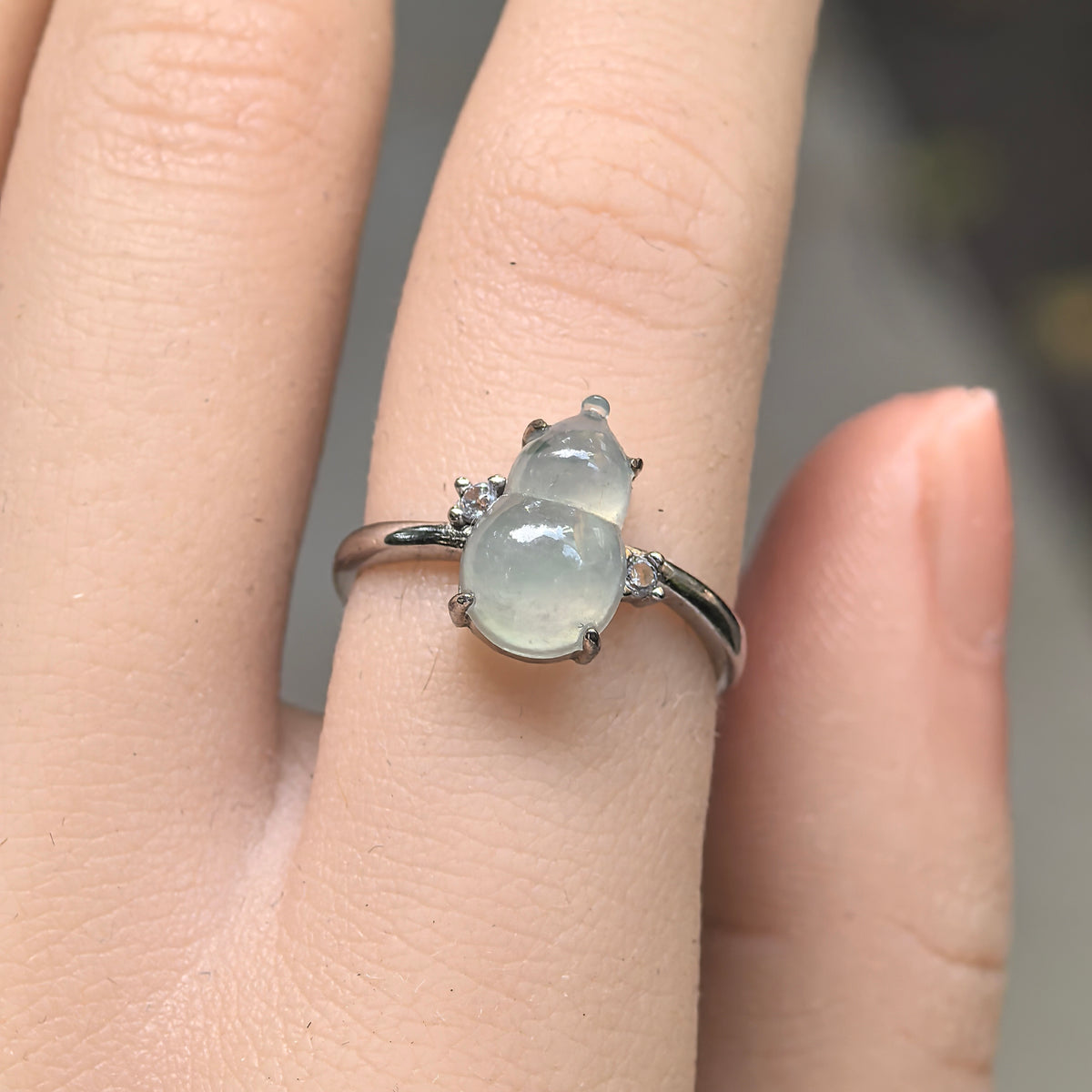 Front view of a pale green jadeite gourd ring worn on a finger, with two round clear accent stones and a slender S925 silver ring band.