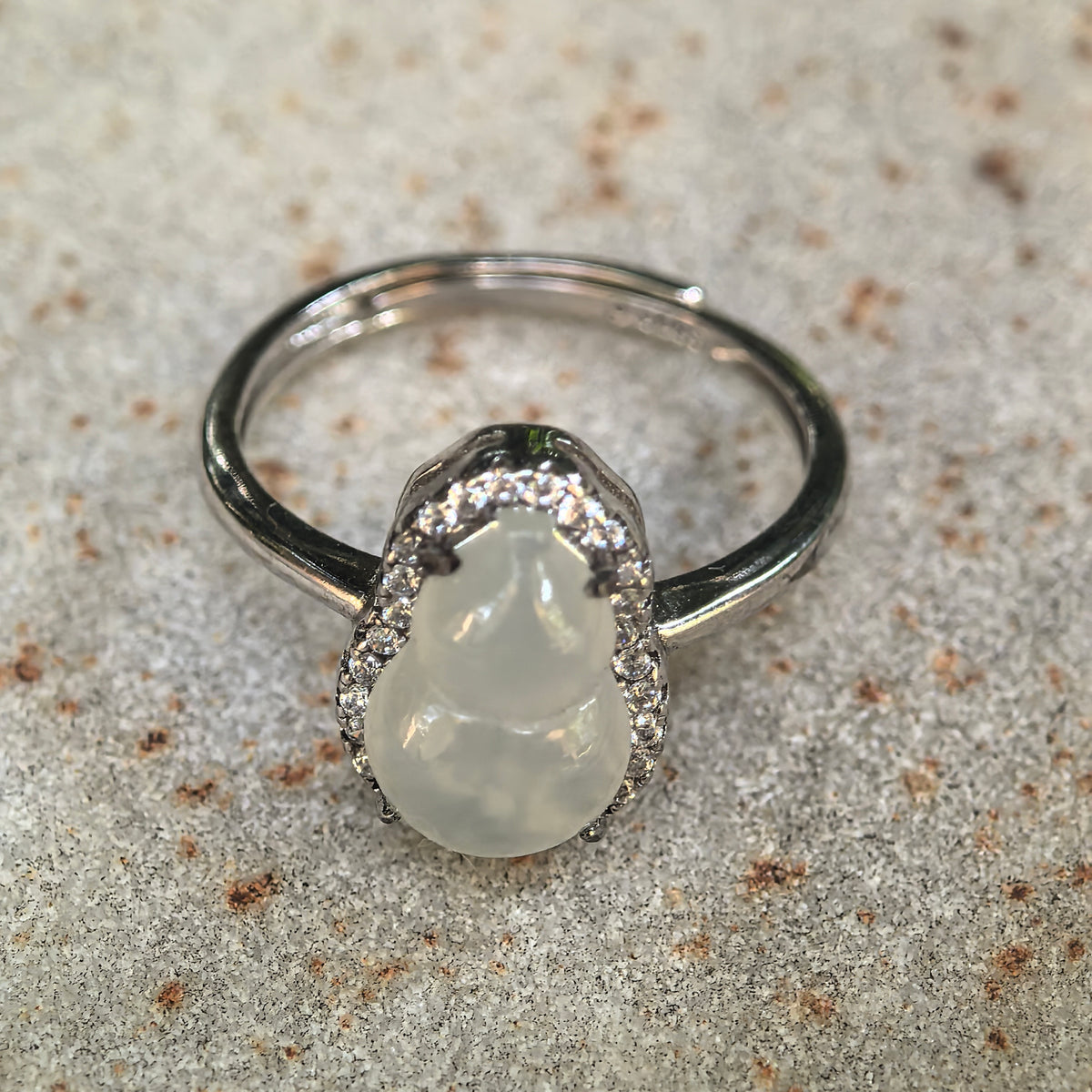 Close-up of the white jadeite gourd ring on stone, with natural snowflake-like inclusions visible inside the carving and the open ring band behind it.