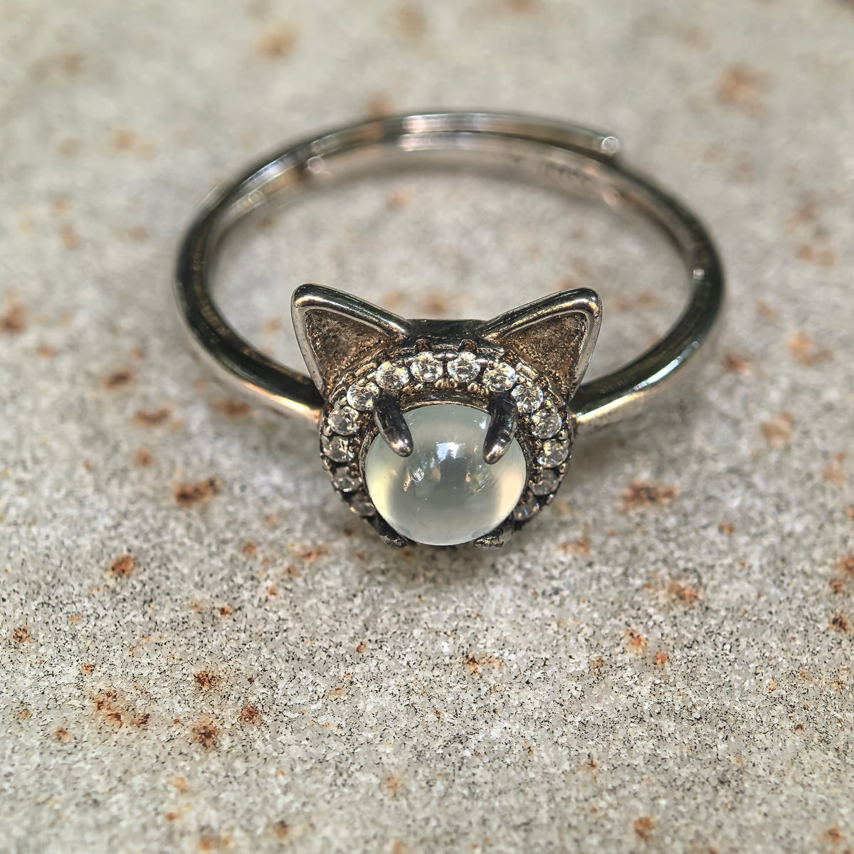 Close-up of the white jadeite cat ring on stone, highlighting the domed cabochon, pointed silver ears and surrounding clear accent stones.