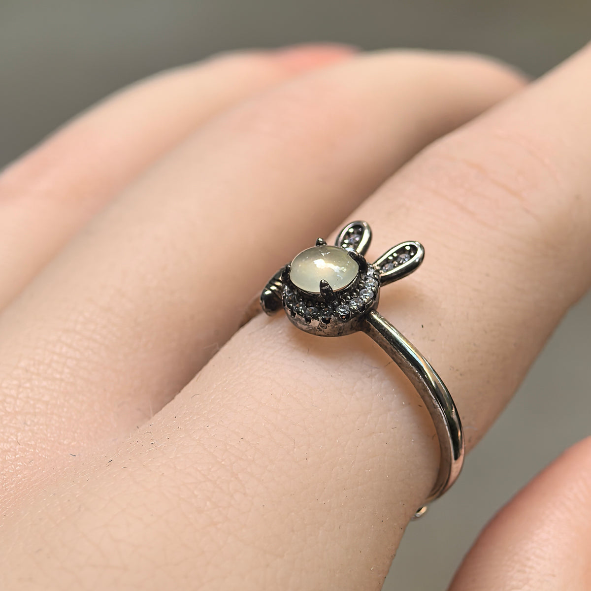 Angled view of a white jadeite rabbit ring worn on a finger, showing the round cabochon, clear accent halo and S925 silver rabbit ears.